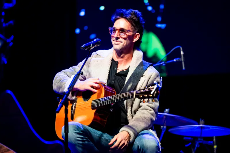 Jake Owen performing live at CoreyFest 2024, sitting with an acoustic guitar on stage at House of Blues Boston with blue stage lighting