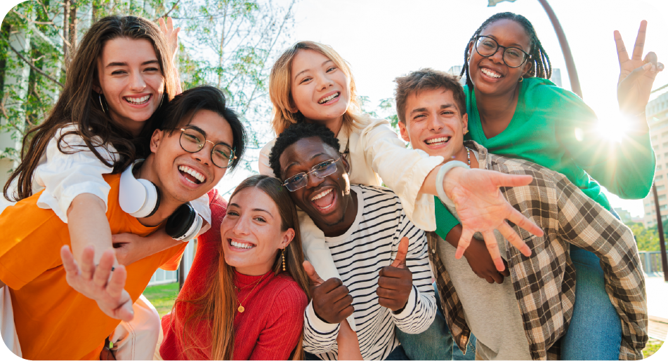 Diverse group of seven young people smiling and posing together outdoors with sun flare in the background, representing Global Nomads Group's mission of connecting youth globally