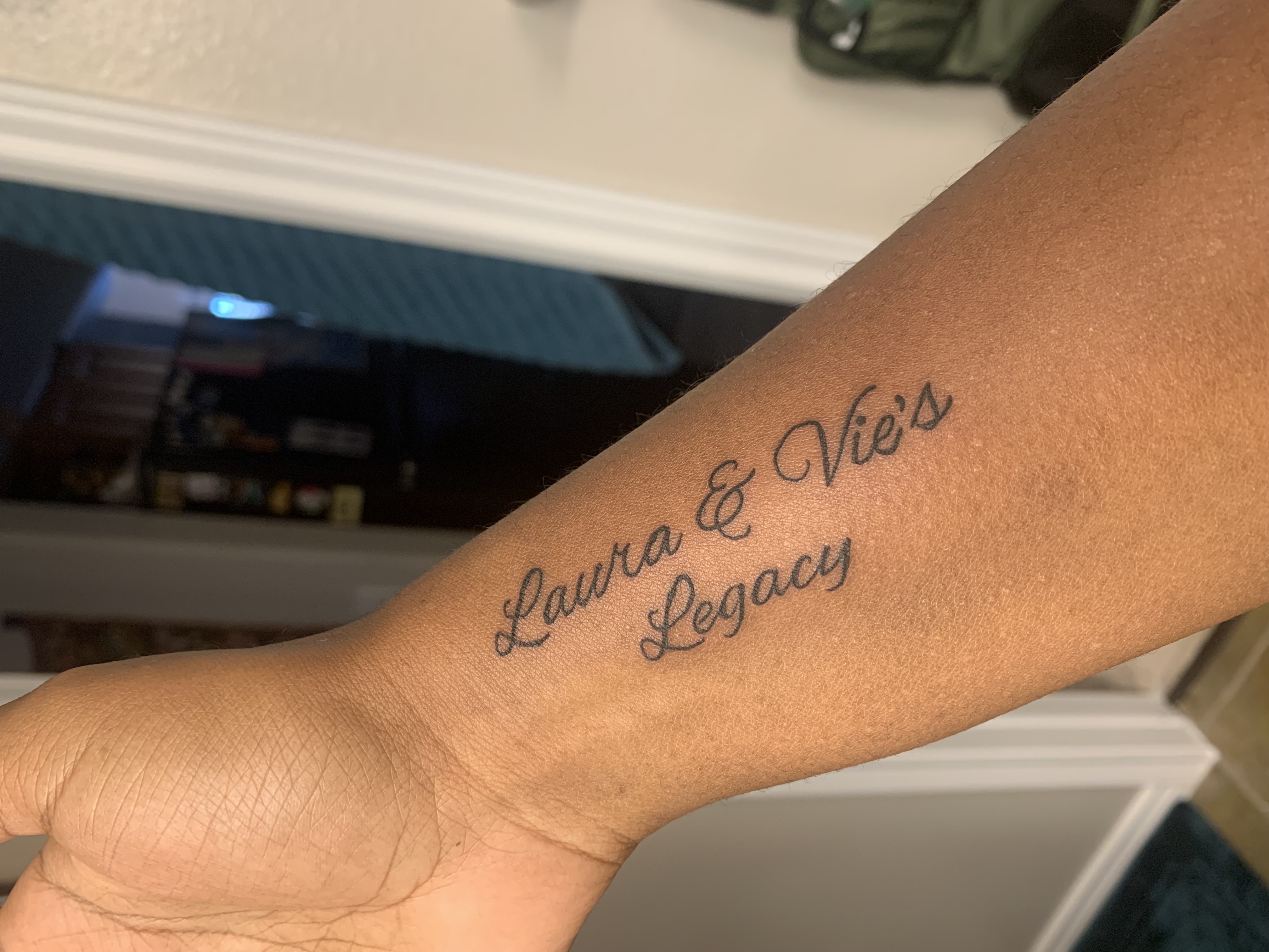 Janelle's wrist tattoo reading 'Laura & Vie's Legacy' in elegant cursive script